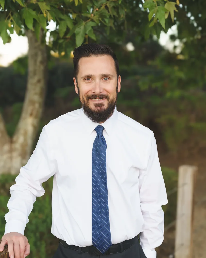 Kyle D. Smith, California employment attorney, in shirt and tie, leaning on a fence post